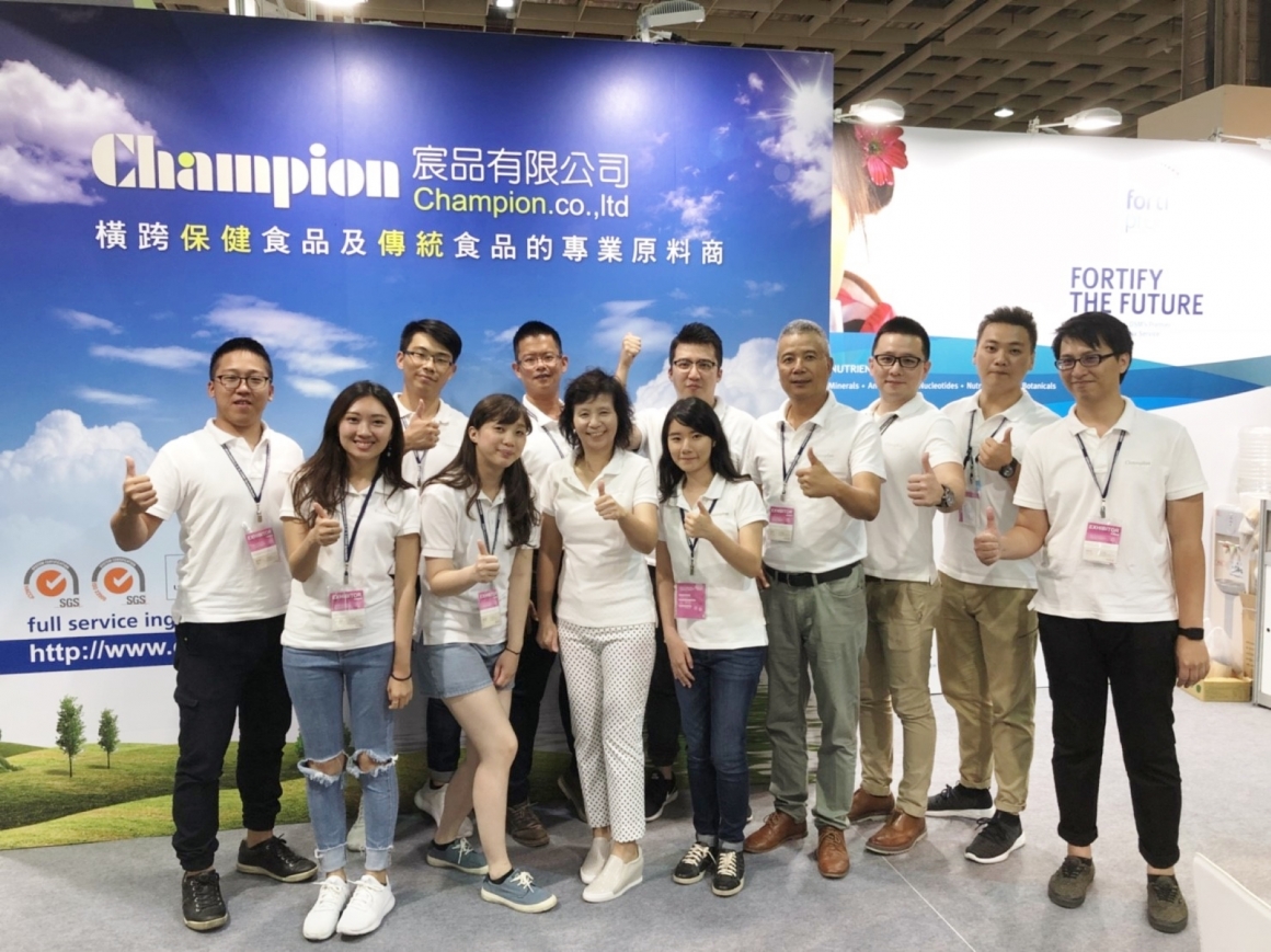 Group picture of Champion employees with raised thumbs in front of exhibition stall