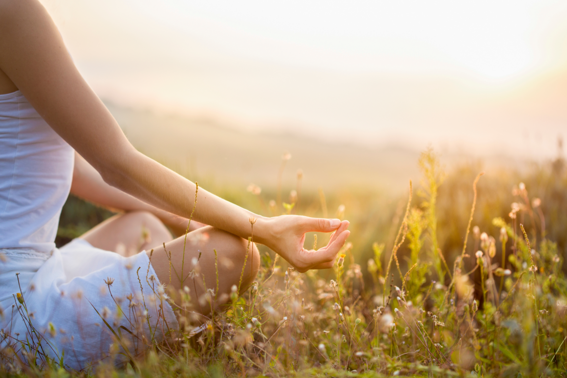 Woman in white clothes sitting and meditating in a lush meadow