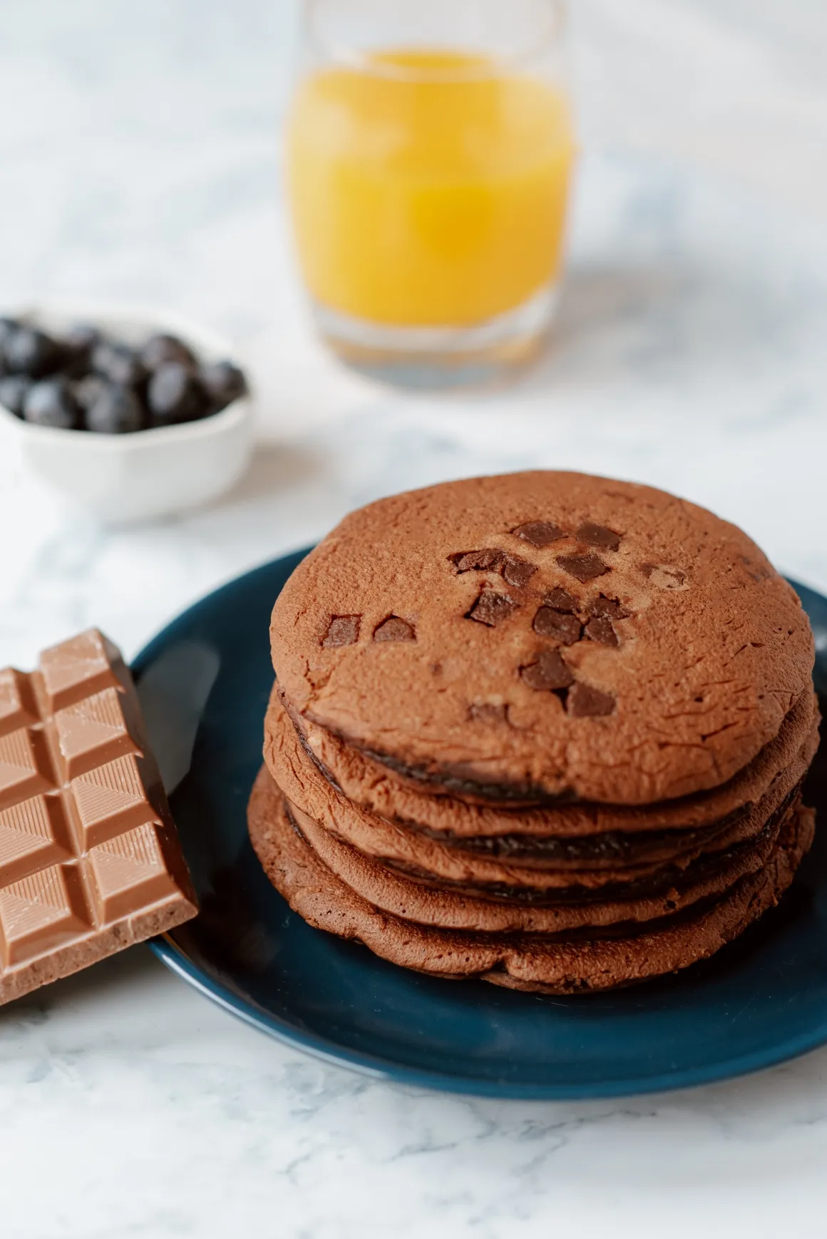 Pile of brown pancakes on a plate next to a chocolate bar