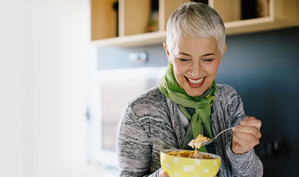 Middle-aged woman smiling while eating cereal from a bowl