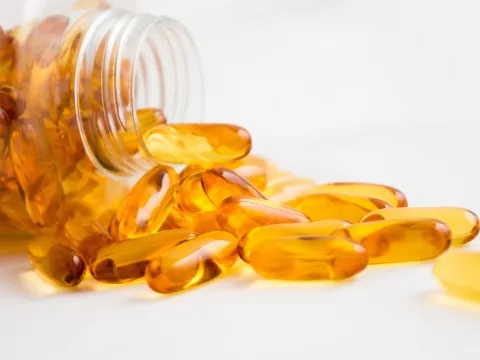 Multiple orange sofgel capsules next to a lying bottle filled with capsules