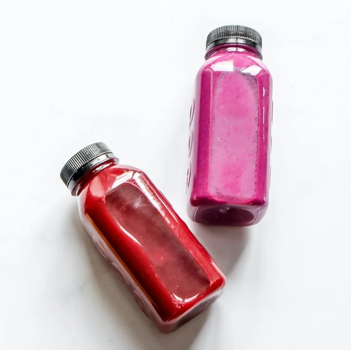 Two bottles with pink content on white surface