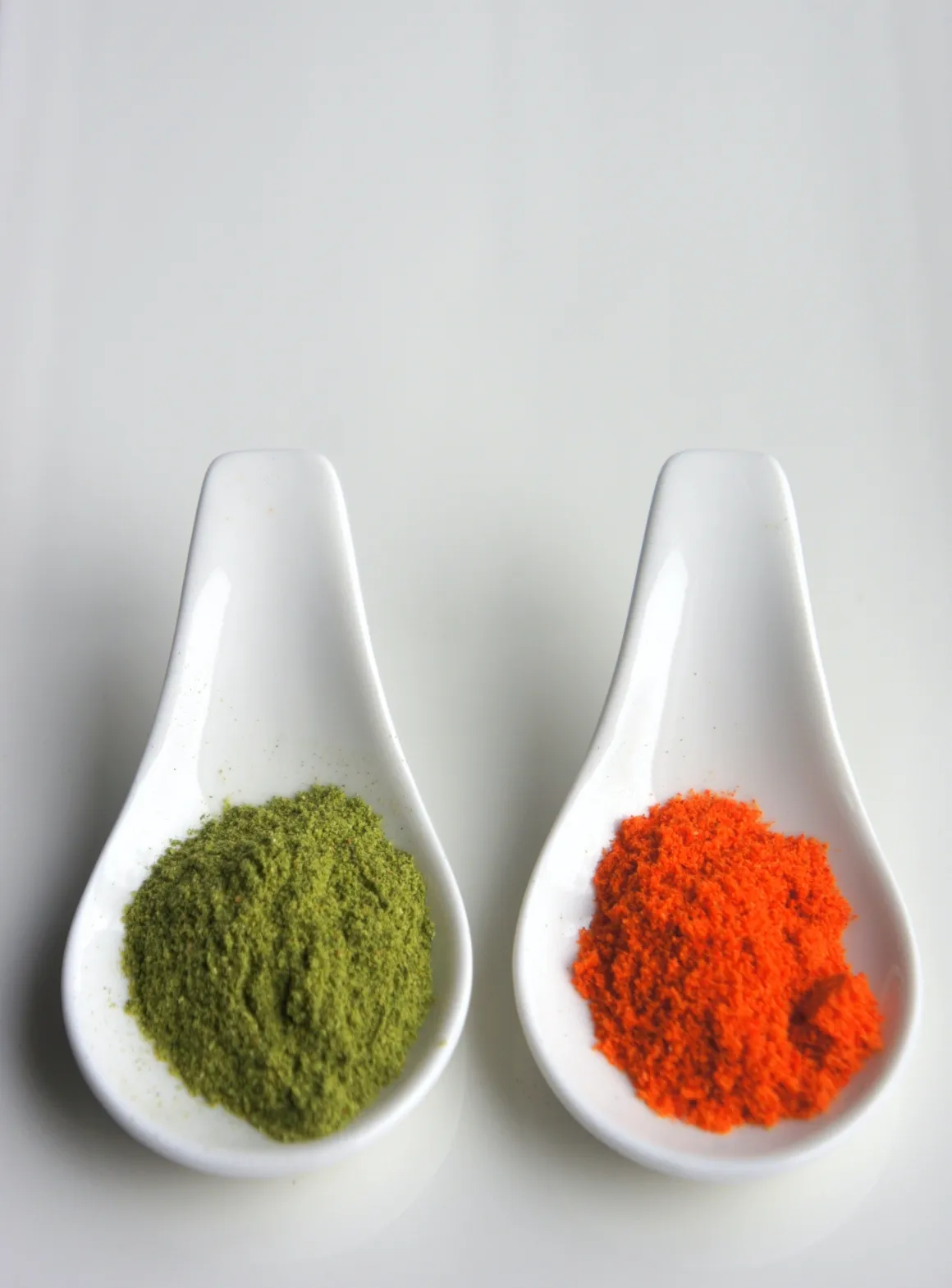 Two ceramic spoons showing a red and a green powder