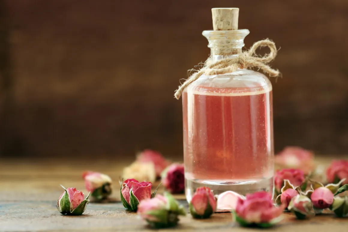 Delicate vial filled with pink liquid surrounded by small rosebuds