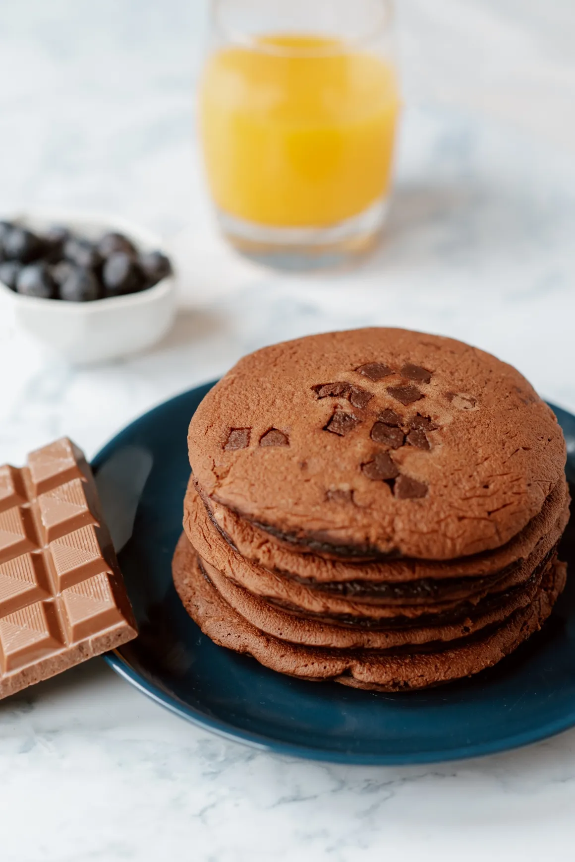 A pile of bown pancakes on a plate next to a bar of chocolate 