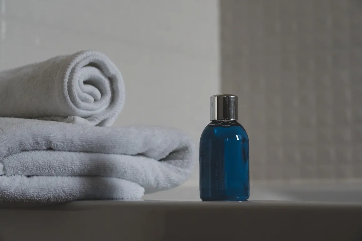 Unlabeled shampoo bottle in front of folded white towels