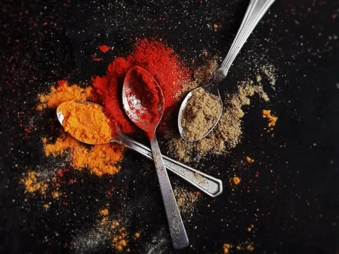 Bright red, orange and green spice powder on three spoons and scattered around on dark surface