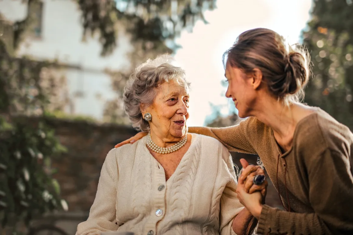 Woman holding an elderly woman's hand and putting her arm around her