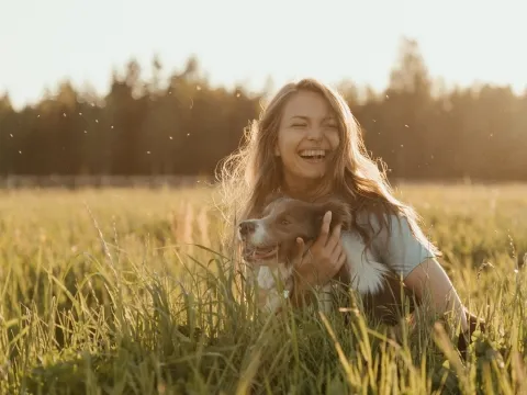 Happy looking young woman hugging her dog on a meadow