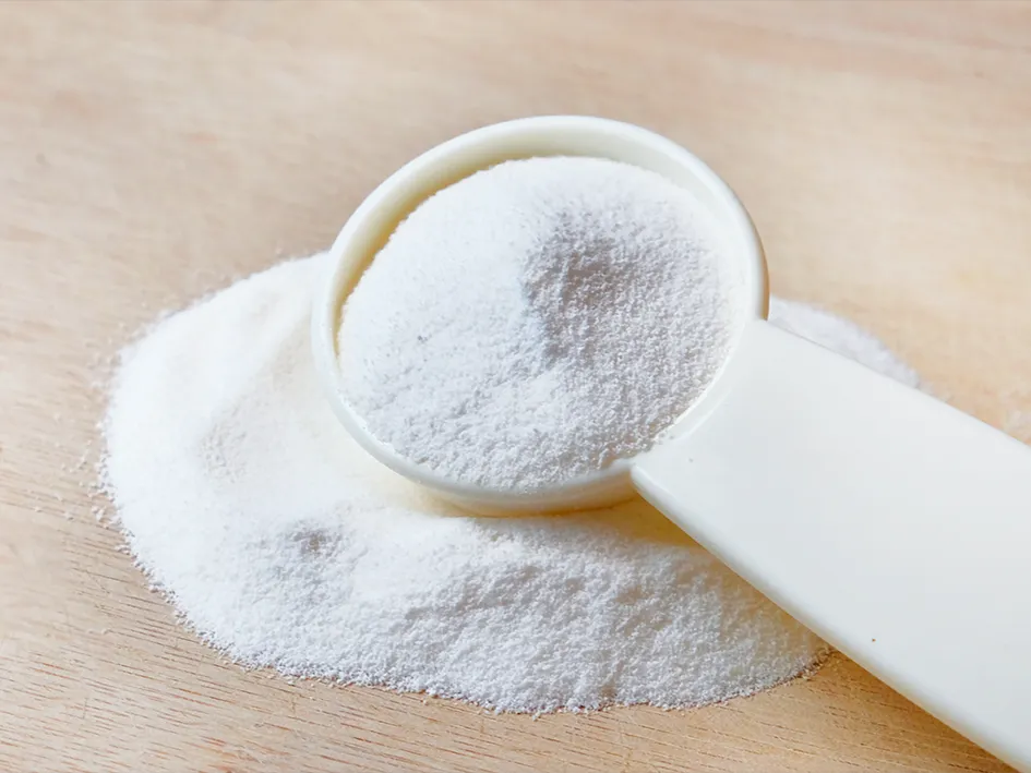 A pile of white kombucha powder and a measuring spoon with powder on a wooden surface