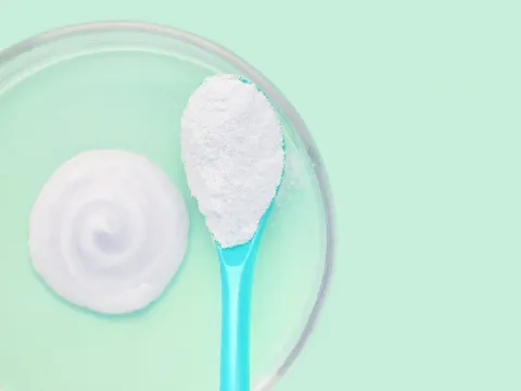 A spoon with a fine white powder next to a blotch of white lotion in a petri dish