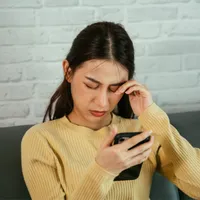 Woman rubbing her eye with one eye looking at her phone