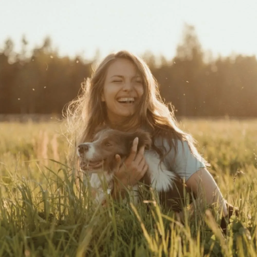 Happy looking young woman hugging her dog on a meadow