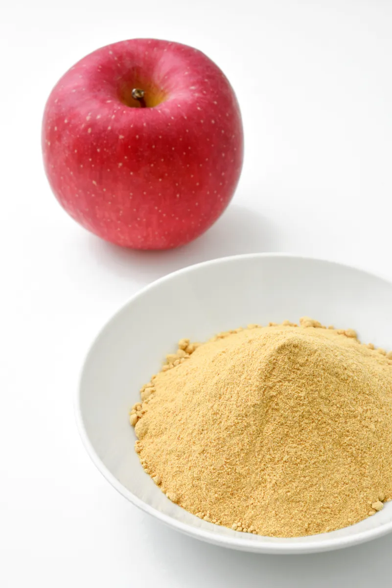 A red apple next to a bowl with fine yellow powder