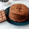 Pile of brown pancakes on a plate next to bar of chocolate