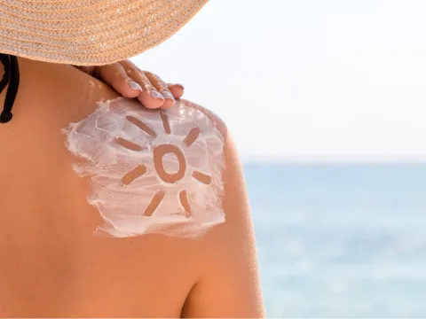 Woman near the seaside with shape of a sun drawn in sunlotion on her shoulder