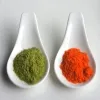 Two ceramic spoons showing a green and bright orange powder