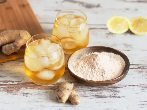 A glass of iced kombucha next to a bowl filled with kombucha powder, sliced lemons and ginger
