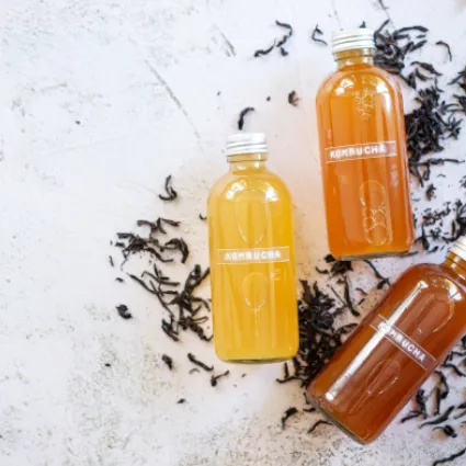 Three bottles labelled kombucha lying on a table with some dried tea leaves