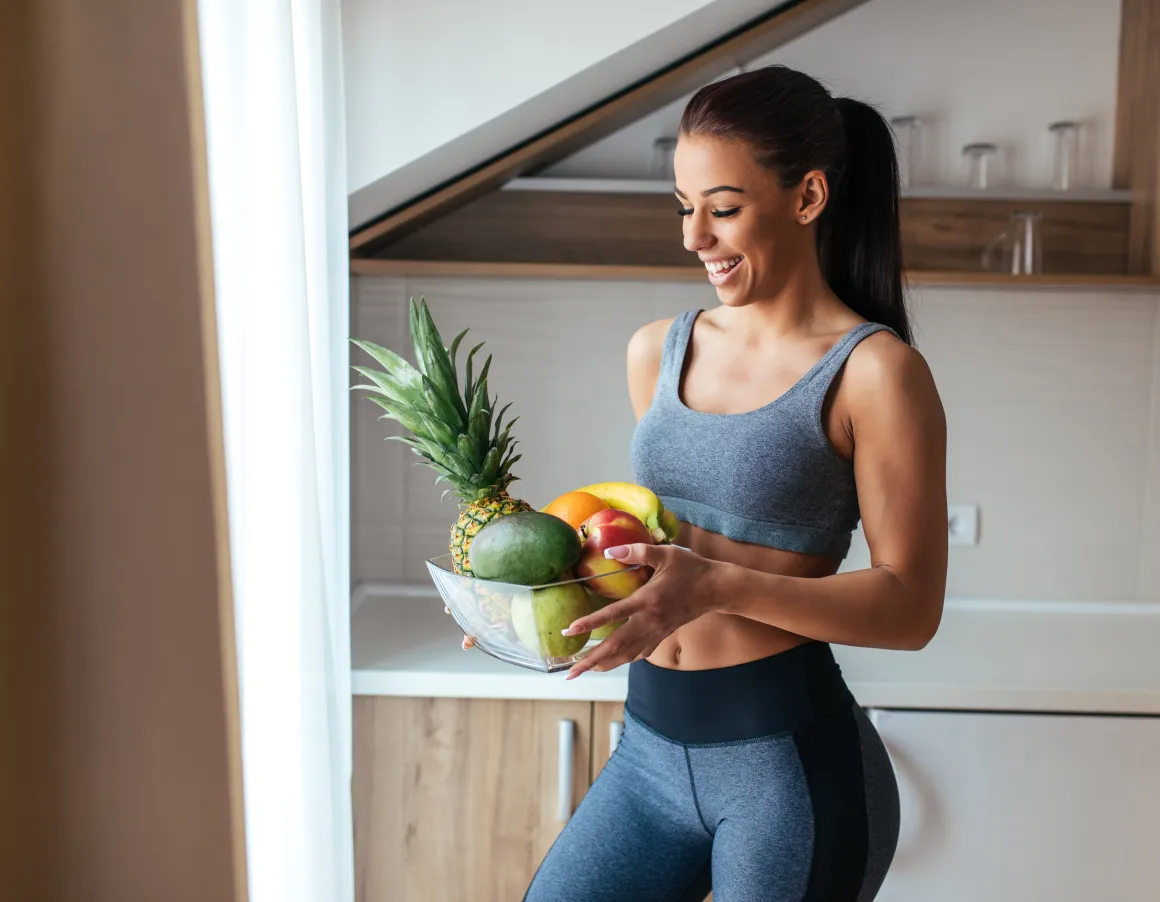 Woman in sports attire holding a bowl of fruits