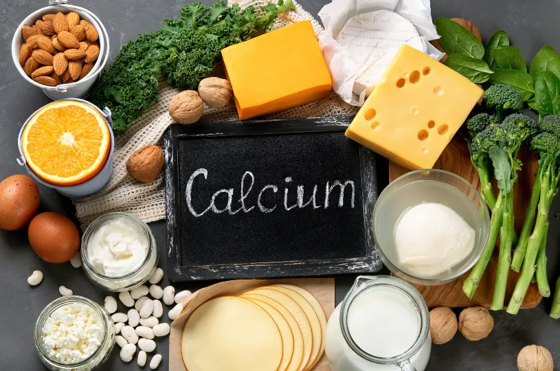 Multiple bowls with cheese, nuts, grains and milk around a small blackboard spelling calcium
