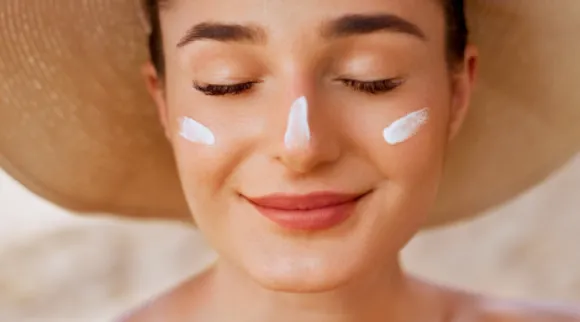 Women in straw hat smiling with eyes closed with white lotion on her nose and cheeks