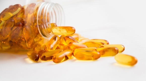 Multiple orange softgel capsules pouring out from a jar