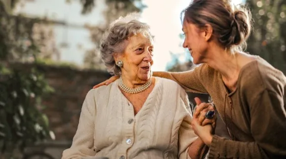 Woman putting her arm around an elderly woman and smiling at her