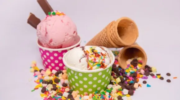 Cups of ice cream among colorful sprinkles and marshmallows