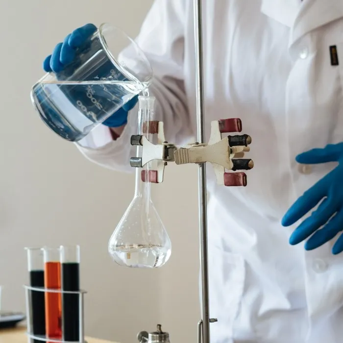 Person in lab coat puring liquid into a chemical flask