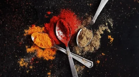 Three spoons with colorful red orange and green spice powder