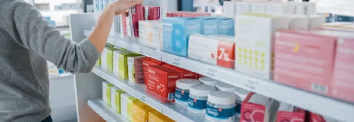 A woman in grey choosing supplement products at a pharmacy.