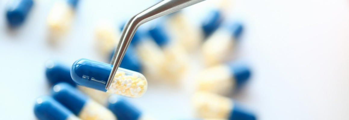 Pharmacist holding a pill with tweezers in a close-up view, showcasing the precision of a low moq supplement manufacturer.