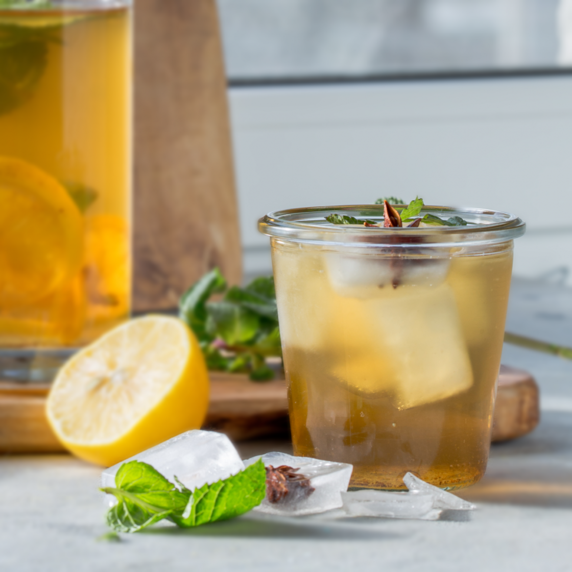 Glass of iced kombucha amidst mint leaves and sliced lime