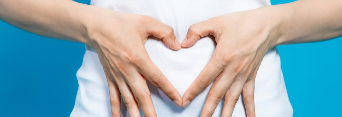 Image of a woman's hands making a heart shape around her abdomen